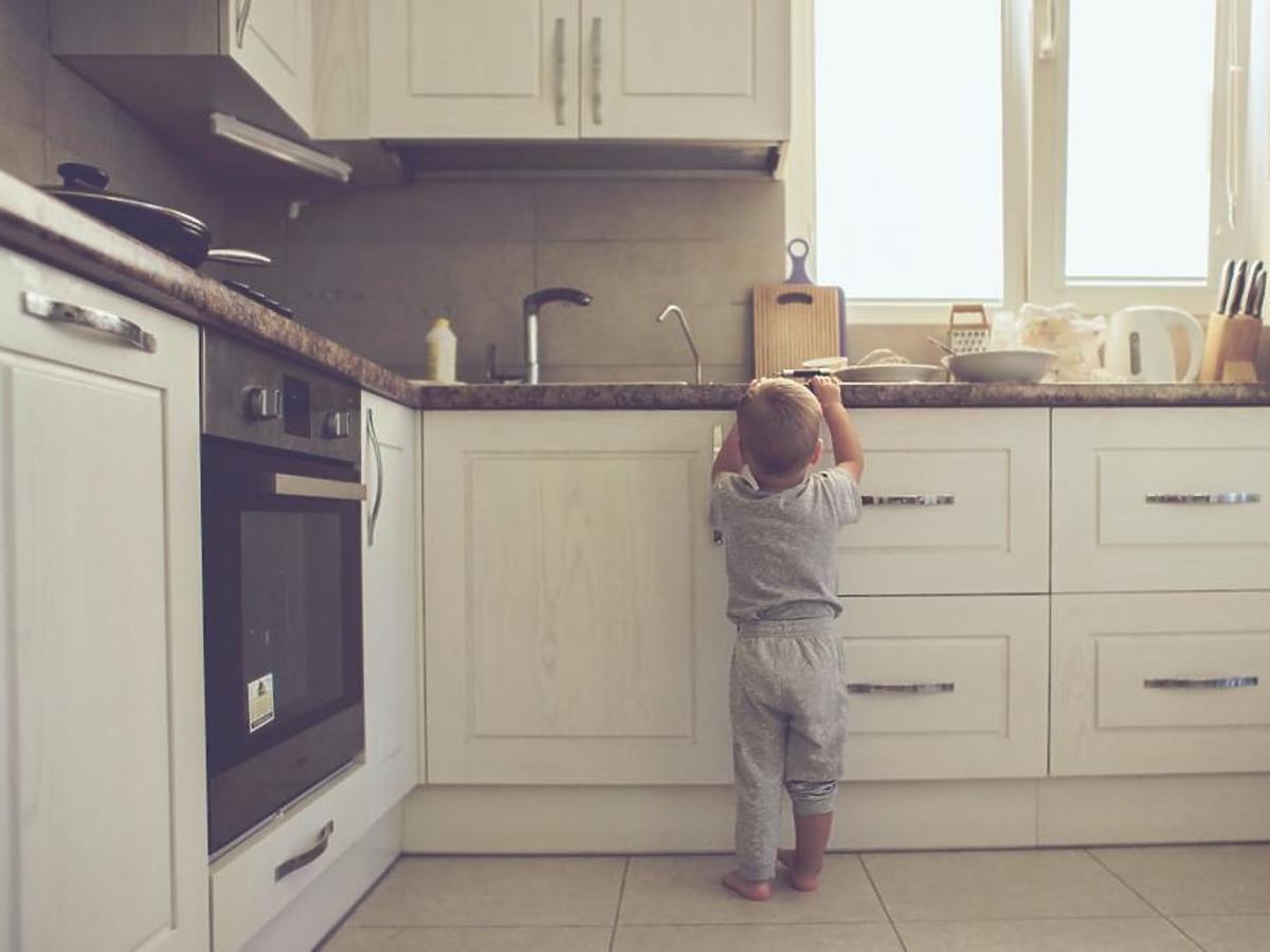2-letni chłopiec sam w domu próbuje zdjąć coś z kuchennej szafki