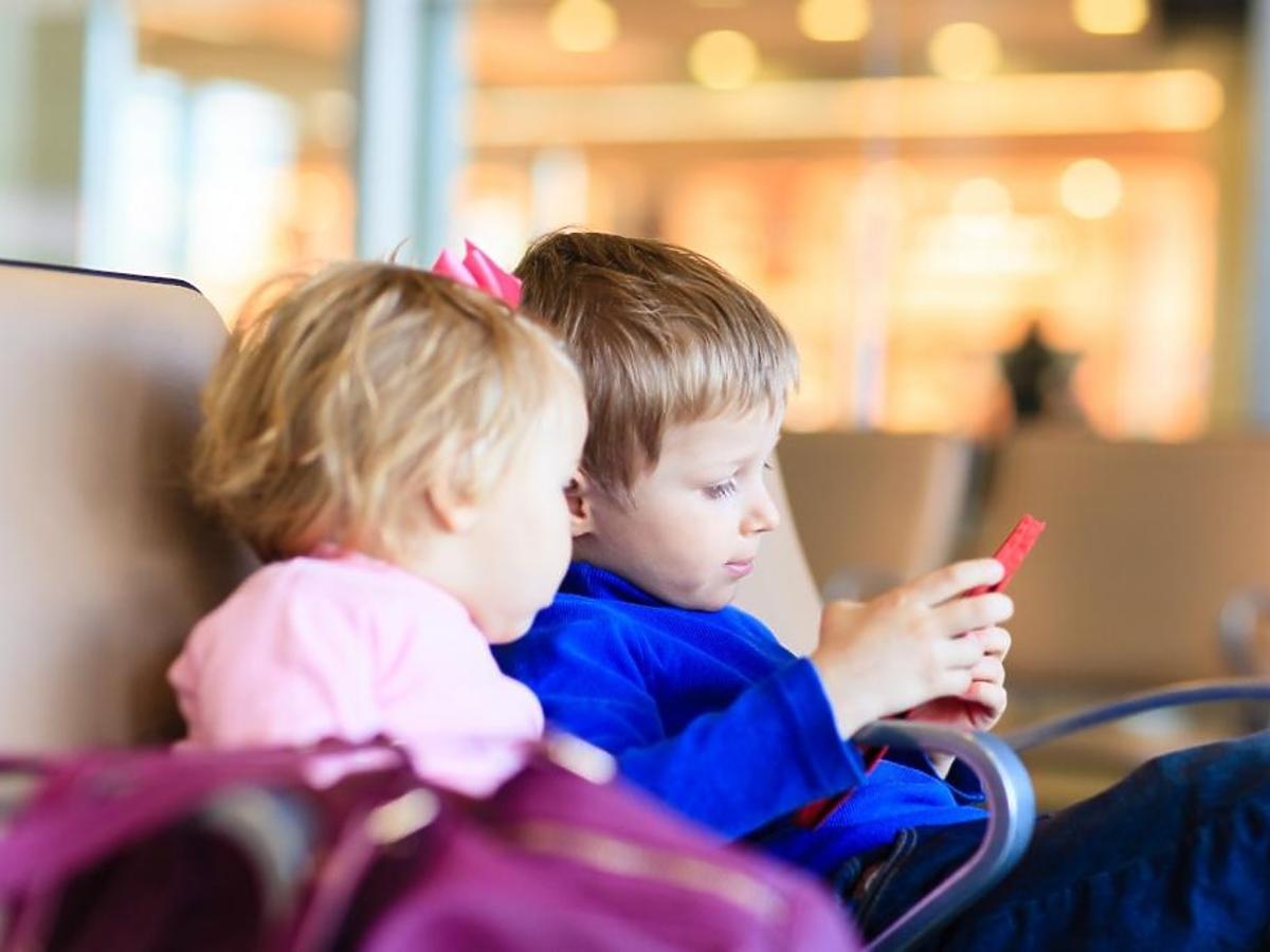 Chłopiec i dziewczynka siedzą wpatrzeni w ekran smartfonu
