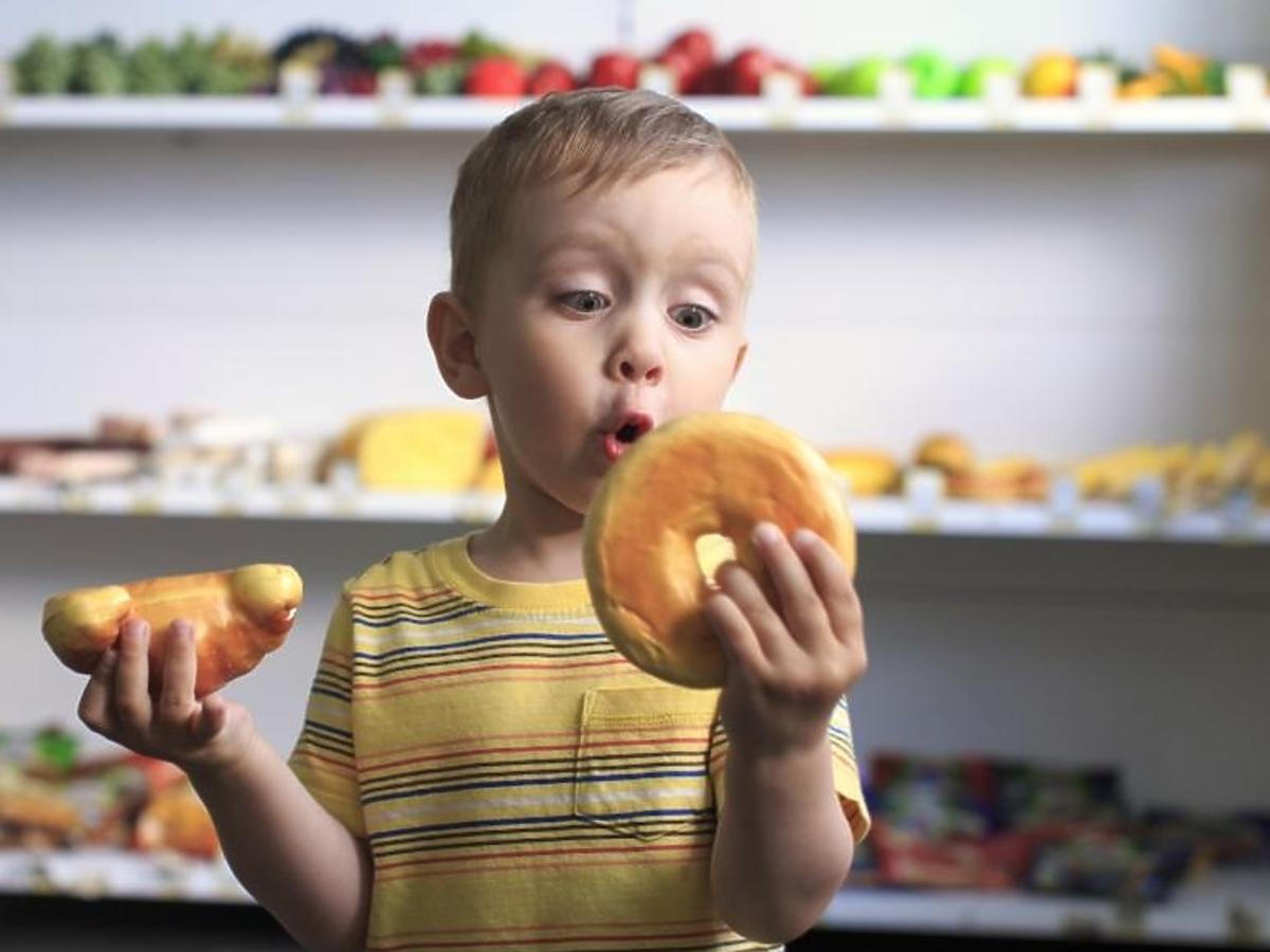 Chłopiec zastanawia się co zjeść: rogalika czy donuta