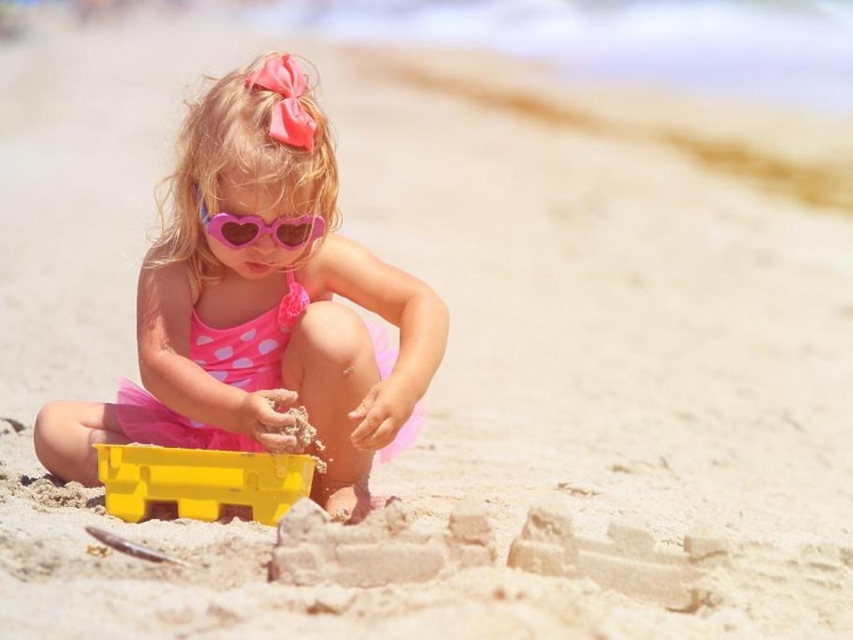 Dziewczynka w okularach przeciwsłonecznych bawi się sama na plaży