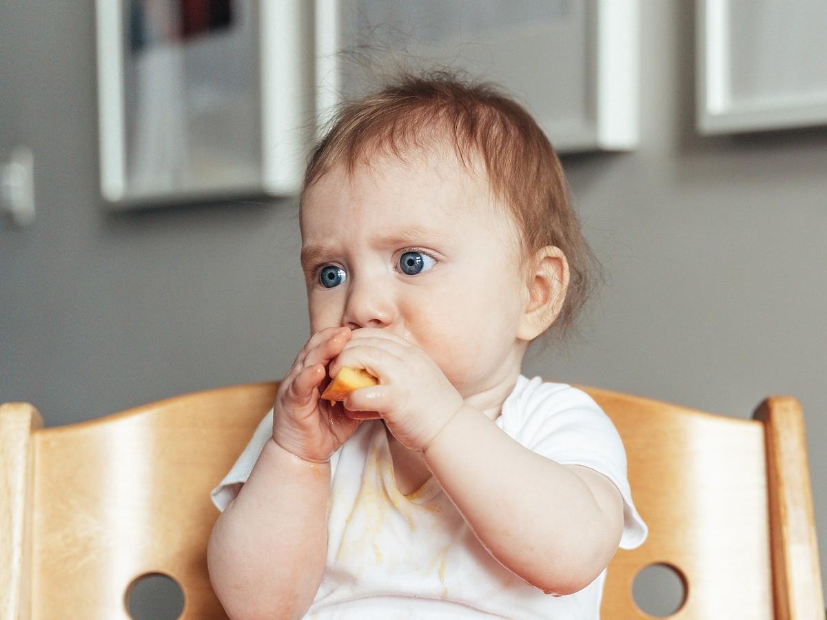 9-miesięczne dziecko je cząstki owocu zgodnie ze schematem rozszerzania diety