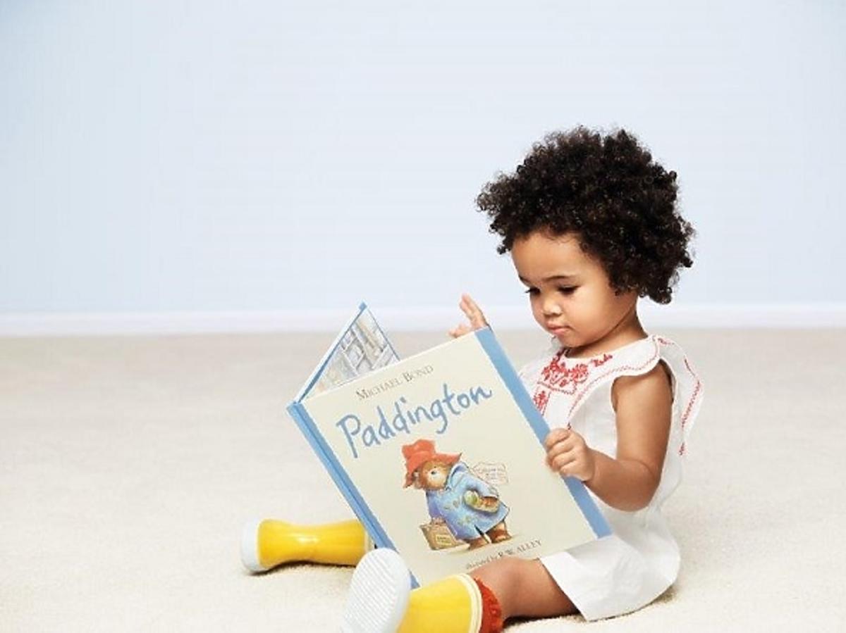 Dziewczynka czytająca książkę ubrana w strój z kolekcji Miś Paddington/ BabyGAP