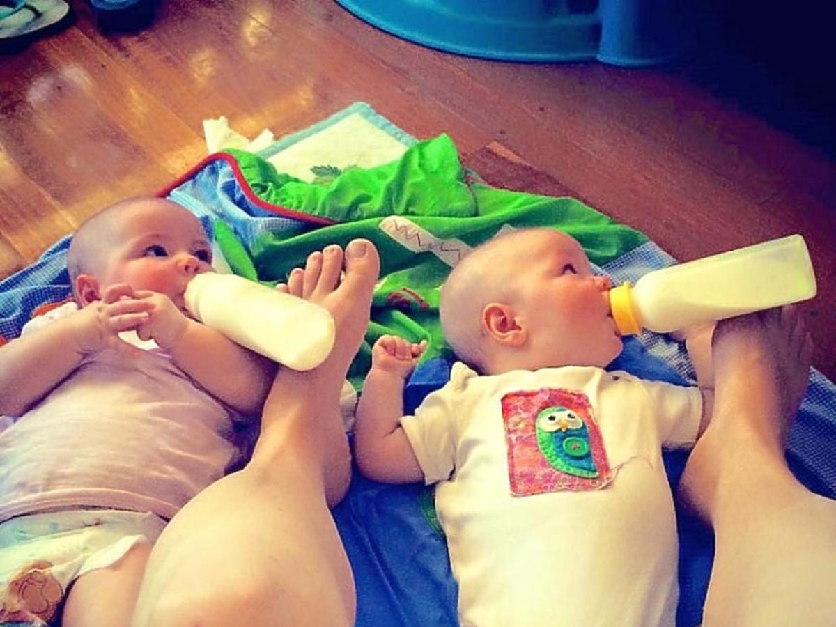Matka karmi bliźnięta przytrzymując butelki stopami