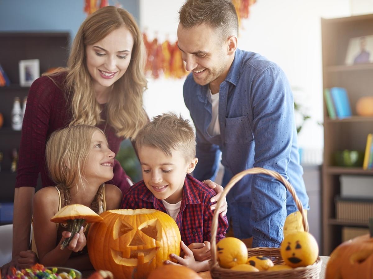 rodzice z dziećmi wspólnie wycinają wzory na dyni w halloween