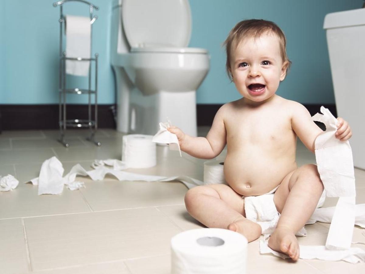 Niegrzeczny chłopiec siedzi na podłodze w łazience wśród sterty papieru toaletowego