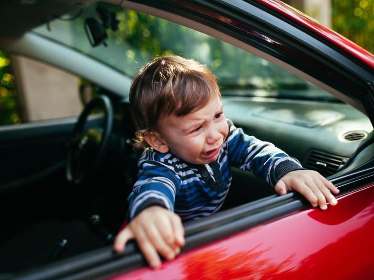 Płaczący chłopiec próbuje wyjść z samochodu przez okno