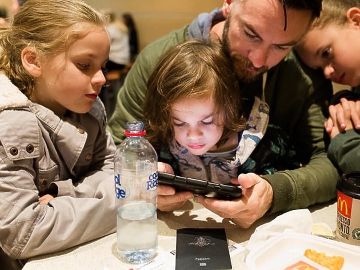 Tata z dziećmi grają na smartfonie i jedzą kolację z McDonald's