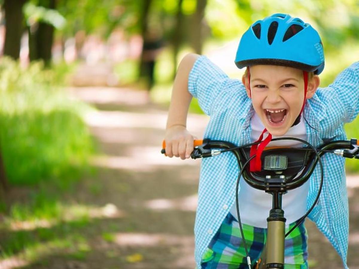 Wesoły chłopiec jedzie w parku rowerem