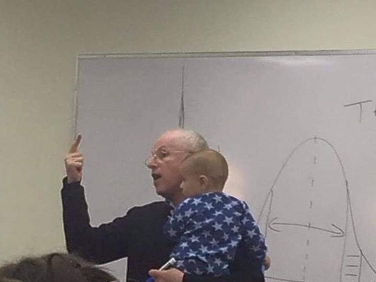 Wykladowca z dzieckiem w ramionach kontynuuje wykład